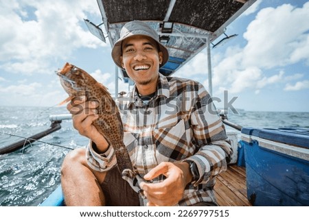 smiling Asian angler holding a grouper on a small fishing boat Royalty-Free Stock Photo #2269797515