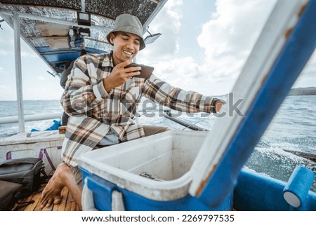fishermen take pictures of the contents of a fish box with a cell phone camera on a small fishing boat