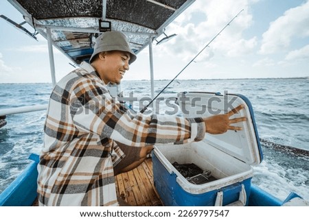 Asian angler opens bait box while fishing with small fishing boat Royalty-Free Stock Photo #2269797547