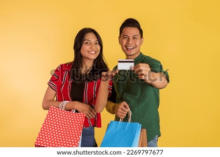 asian couple showing the blank card while holding the shopping bags on orange isolated background