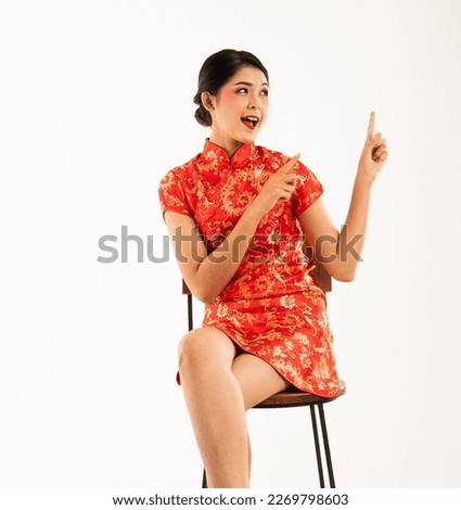 a beautiful asian woman in red cheongsam sitting and pointed to her side with her forefinger Royalty-Free Stock Photo #2269798603