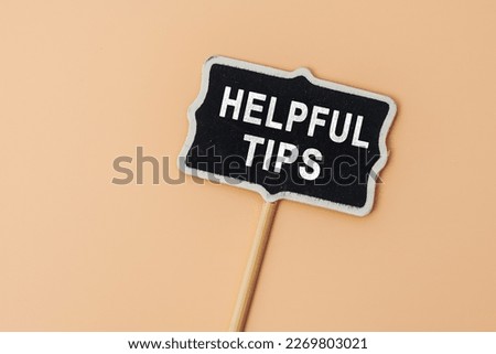 Helpful Tips - text on a small chalkboard on a beige background. Top view. Business, tips and tricks concept