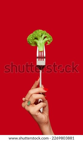 Female hand holding broccoli on fork against red studio background. Healthy eating. Food pop art photography. Concept of art and creativity. Complementary colors. Copy space for ad, text Royalty-Free Stock Photo #2269803881