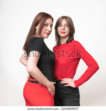 Adult mother in black t-shirt and red trousers, teenager daughter on contrary in red t-shirt and black trousers. Togetherness concept. Studio shot on white background. Part series. Human Connections Royalty-Free Stock Photo #2269808097