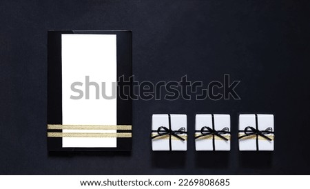 black envelope mockup, shot from the top on a black background with copy space. Tied with a gold ribbon. Three Gift boxes with ribbon. white blank card for text. Business invitation, Father's Day.