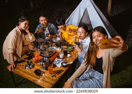 a group of people taking a groufie photo at the camp site while eating the grilled beef