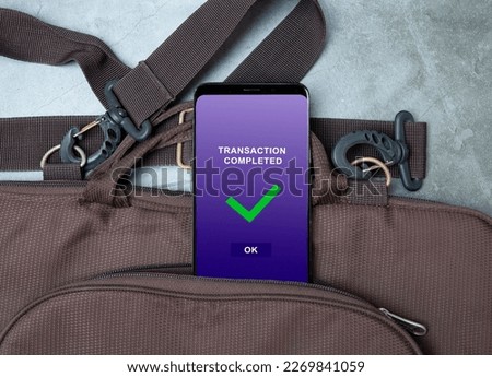 transaction completed notification in a mobile phone screen, phone alongside with bag on table