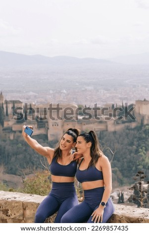 Sporty twin sisters take a selfie with the Alhambra in Granada Spain in the background