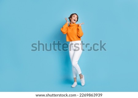 Full body photo of attractive young woman astonished hands look empty space wear trendy orange garment isolated on blue color background