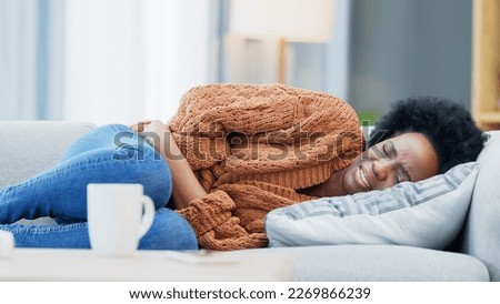 Woman with menstruation stomach cramps and belly ache holding her sore tummy while feeling ill on a sofa at home. Hungry female with period getting sick, bloated and uncomfortable with digestive pain Royalty-Free Stock Photo #2269866239