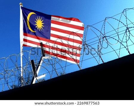 The Malaysian flag hangs in the cloudy sky outside the prison's barbed wire. waving in the sky