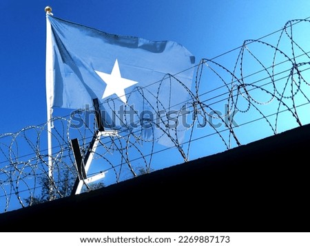 The Somalia flag hangs in the cloudy sky outside the prison's barbed wire. waving in the sky