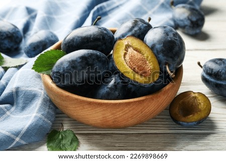 Napkin and bowl of plums on wooden background
