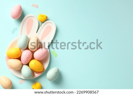 Colorful Easter eggs on plate with bunny ears on pastel blue background. Flat lay, top view, copy space.