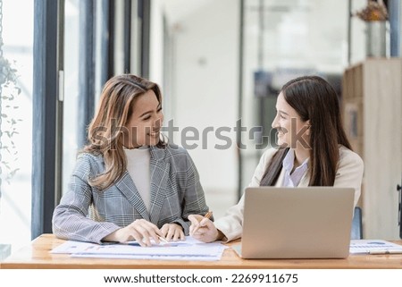 Two beautiful Asian businesswoman in conversation Exchange ideas at work Company employees working together by talking and guiding each other with papers, graphs and desk laptops.