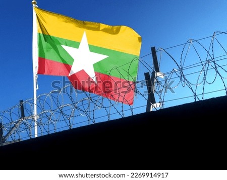 The Myanmar flag hangs in the cloudy sky outside the prison's barbed wire. waving in the sky Royalty-Free Stock Photo #2269914917