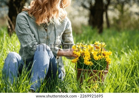 Spring season in nature. Woman with daffodil flowers in wicker basket sitting in grass. Relaxation outdoors Royalty-Free Stock Photo #2269921695