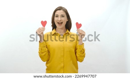 Smiling young woman isolated on white background dancing with two paper hearts she made. Portrait of a smiling woman with two paper hearts. Valentine's or mother's day celebration.