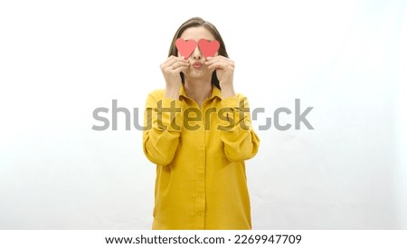 Smiling young woman isolated on white background holding two paper hearts she made in her eyes. Portrait of a smiling woman with two paper hearts. Valentine's or mother's day celebration.