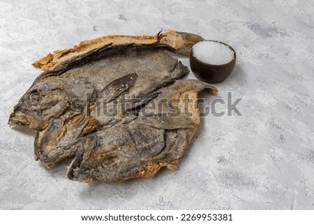 Salted dry raw cod on a light textured background with a well of salt grains