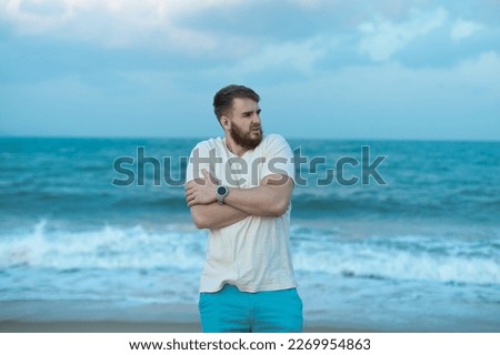 Portrait of unhappy depressed frozen trembling guy, young shivering from cold sad upset man on the sea beach, suffering from bad weather on summer vacation  Royalty-Free Stock Photo #2269954863
