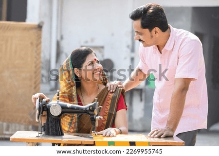 Indian rural woman using sewing machine and her husband.