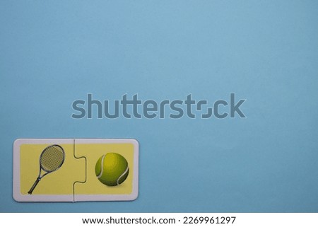 Colorful educational puzzle pieces with pictures of tennis rackets and tennis balls placed on the lower left of a blue background.