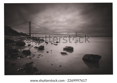 Grey, cloudy, misty picture of rocky shore and bridge
