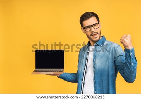 Happy winner! Smiling businessman pointing finger on blank laptop screen isolated over yellow background. Looking at camera.