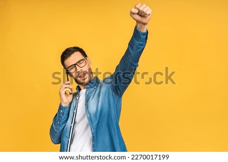 Happy winner. Portrait of casual bearded man with smartphone isolated over yellow background.