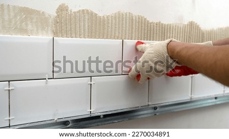 Laying ceramic tiles on the backsplash of the kitchen. A worker lays and installs white ceramic tiles in a kitchen. Ceramic tile-fish. Royalty-Free Stock Photo #2270034891
