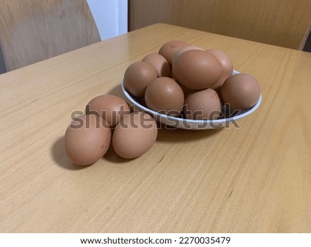 Picture of many eggs in a while bowl on a brown wooden table