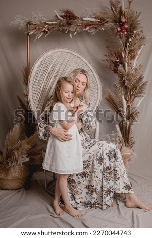 Mommy and me studio photo session sitting on a rattan vintage chair decorated with dried flowers 