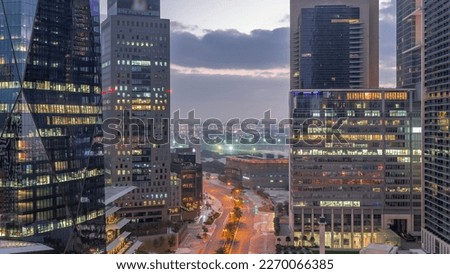 Dubai International Financial district night. Aerial view of business office towers before sunrise. Illuminated skyscrapers with road traffic and Deira district on a background