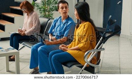 Medical assistant consulting asian woman with crutches, using digital tablet to fill in checkup report and receive healthcare insurance. Patient with physical impairment talking to nurse.