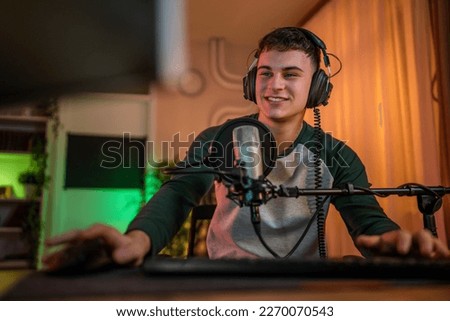 Young man teenager play video games on pc computer while streaming to social media or internet online playtrough walktrough video male gamer having fun at home wear headphone happy winning copy space Royalty-Free Stock Photo #2270070543