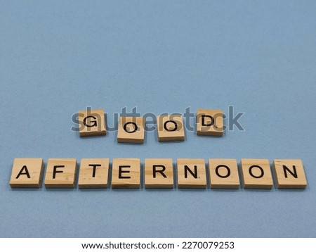 selective focus on the arrangement of the black alphabet in a brown box on a blue background. It forms the writing GOOD AFTERNOON