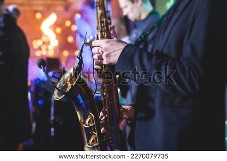 Concert view of saxophonist, a golden saxophone, sax player with vocalist and musical band during jazz orchestra show performing music on a stage in the scene lights
 Royalty-Free Stock Photo #2270079735