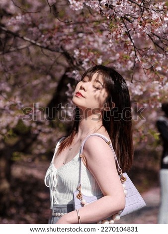 Outdoor portrait of beautiful fashion young Chinese girl posing eyes closed with blossom cherry flowers background in spring garden, beauty, summer, emotion, lifestyle, expression and people concept.