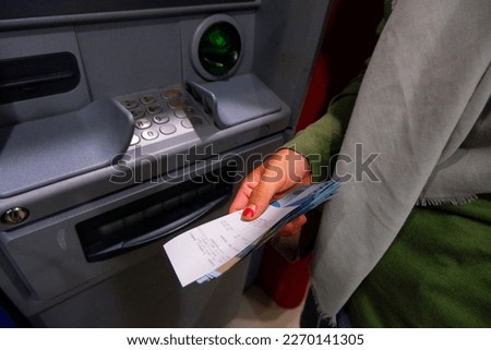 A woman's hand holding a receipt and money from an ATM machine transaction, in a muntok city at night