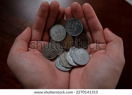 A pile of metal rupiah coins in the palm of an Asian woman, at Belo Laut Village during the day