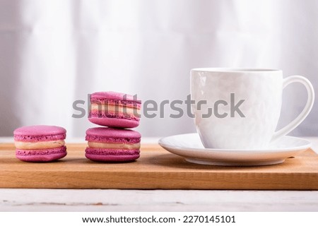 three pink macaroons and a white cup of coffee on a wooden table close-up