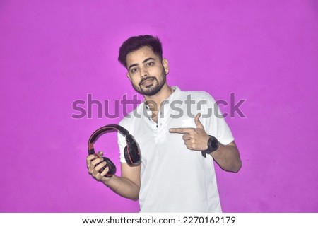 Excited asian woman wear earphones using finger pointing copy space on purple background. Cheerful positive teenager with headphones pointing present shocked promotion display over pastel background.