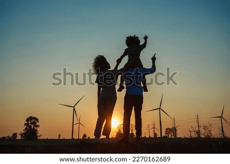 Silhouettes of Happy family father, mother and child daughter sits on the shoulders of his father with windmills for electricity generation at sunrise by producing sustainable energy 