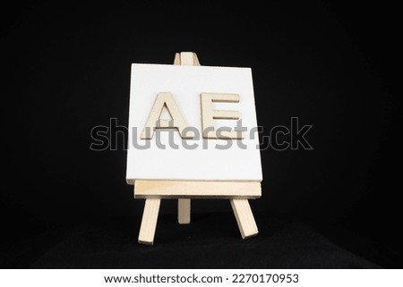 A E wooden capital letter and white blank painting canvas resting on an miniature artists easel isolated on a black background