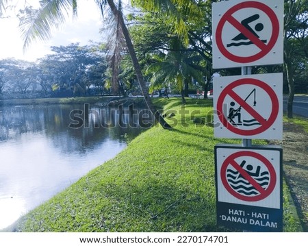 This is a sign prohibiting swimming and fishing, this sign is posted near the lake. this sign adds "No swimming" in Indonesian