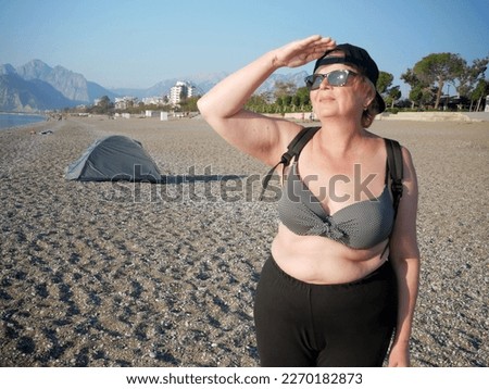 Senior adventure is ageless woman with backpack on sea beach near tent in Antalya Turkey. Summer active tourism for pensioner. Outdoors