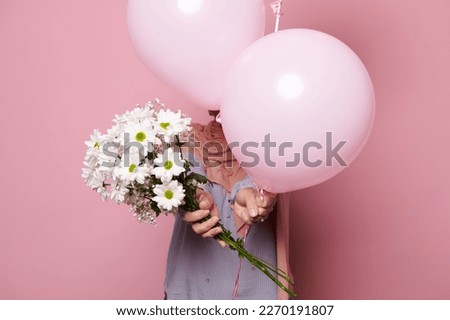 Selective focus on a beautiful bouquet of white spring chamomile flowers and a bunch of pink pastel helium balloons, isolated pink background. Celebration happy festive event. Decoration for birthday