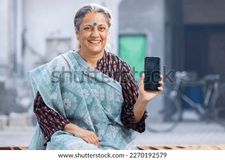 Happy senior woman showing blank empty smart phone screen at home