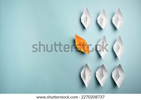 Yellow paper boat floating away from others on light background, flat lay with space for text. Uniqueness concept
